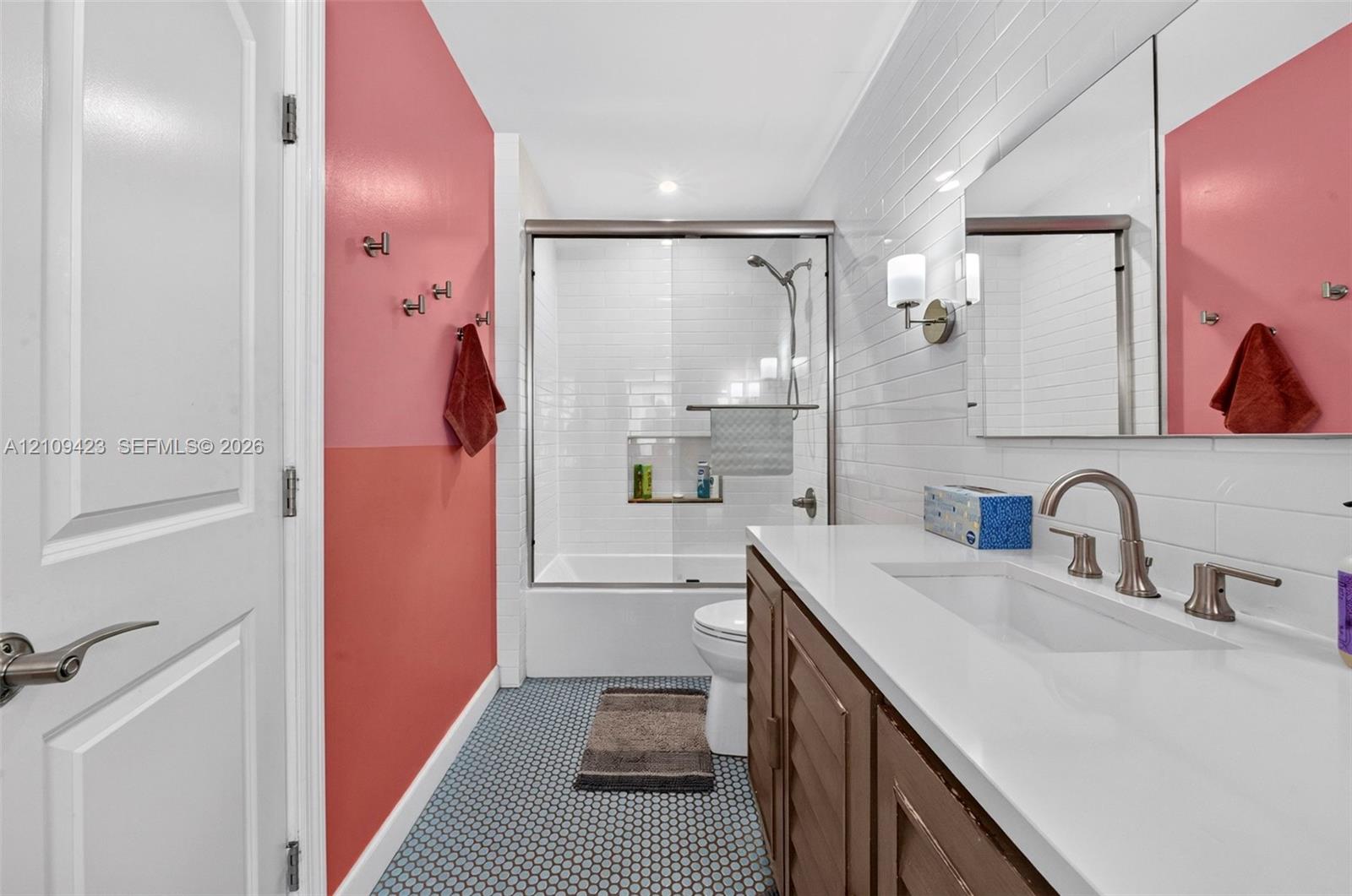 Bathroom featuring a vanity with a white countertop, subway-tiled shower surround, glass-enclosed tub, and hexagonal tile flooring