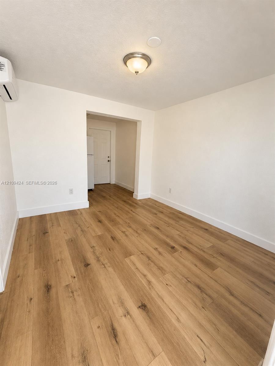Interior space featuring neutral wall tones, wood-finish flooring, a wall-mounted ductless climate control unit, and a flush-mount ceiling light fixture