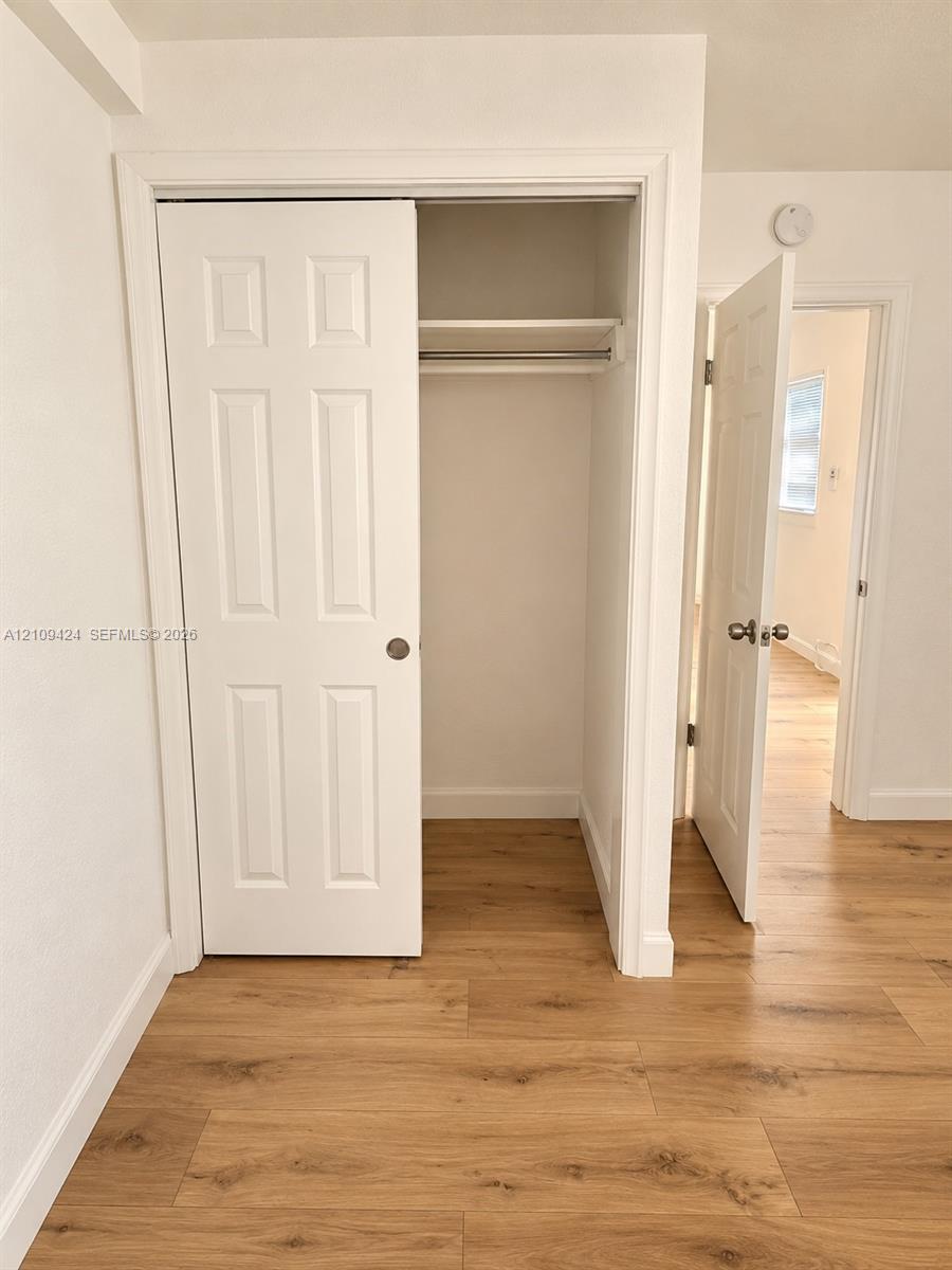 Closet featuring a six-panel door and built-in shelving, complemented by wood-finish flooring