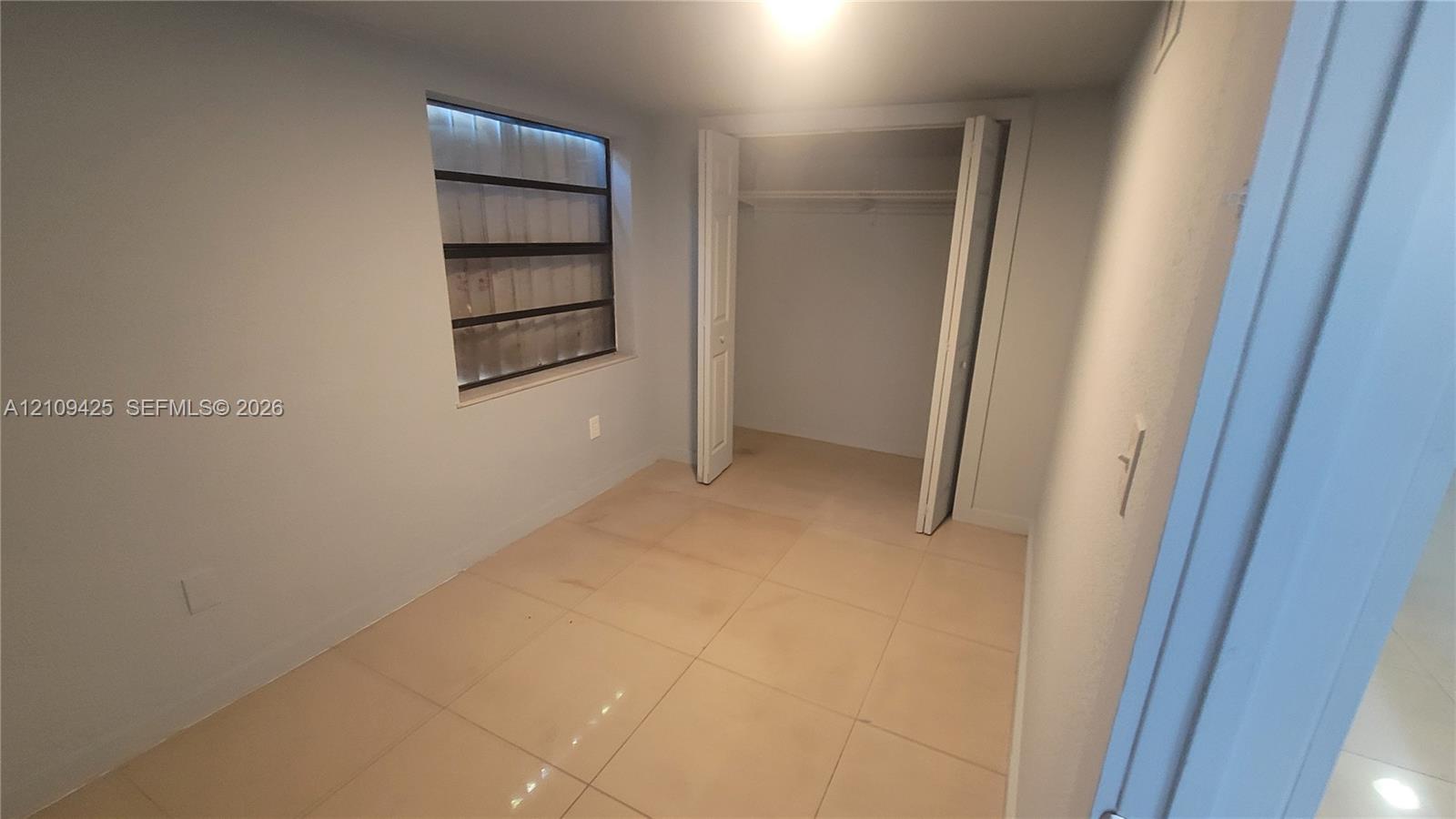 Room featuring large-format ceramic tile flooring, neutral wall paint, a multi-pane jalousie window, and a built-in closet with folding double doors