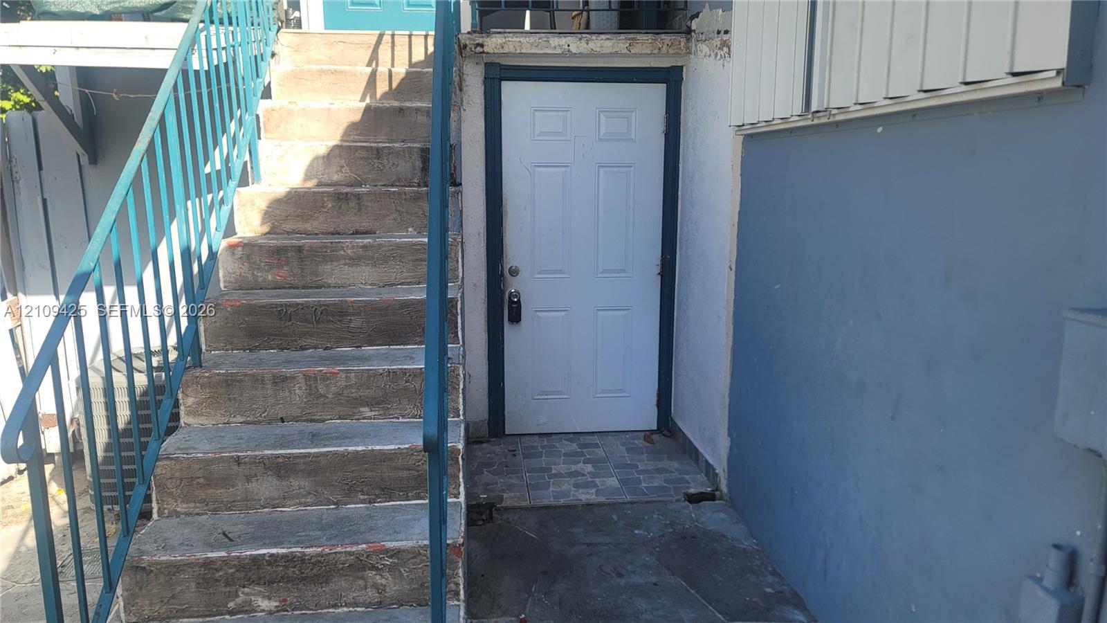 Exterior entry featuring concrete stairs with a metal railing and a multi-panel door with stone-tile flooring at the threshold