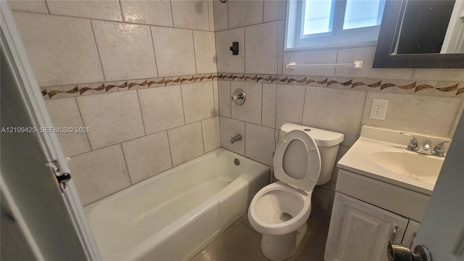Bathroom featuring wall-to-wall ceramic tiling, decorative tile inlay, integrated vanity, and shower-tub combination