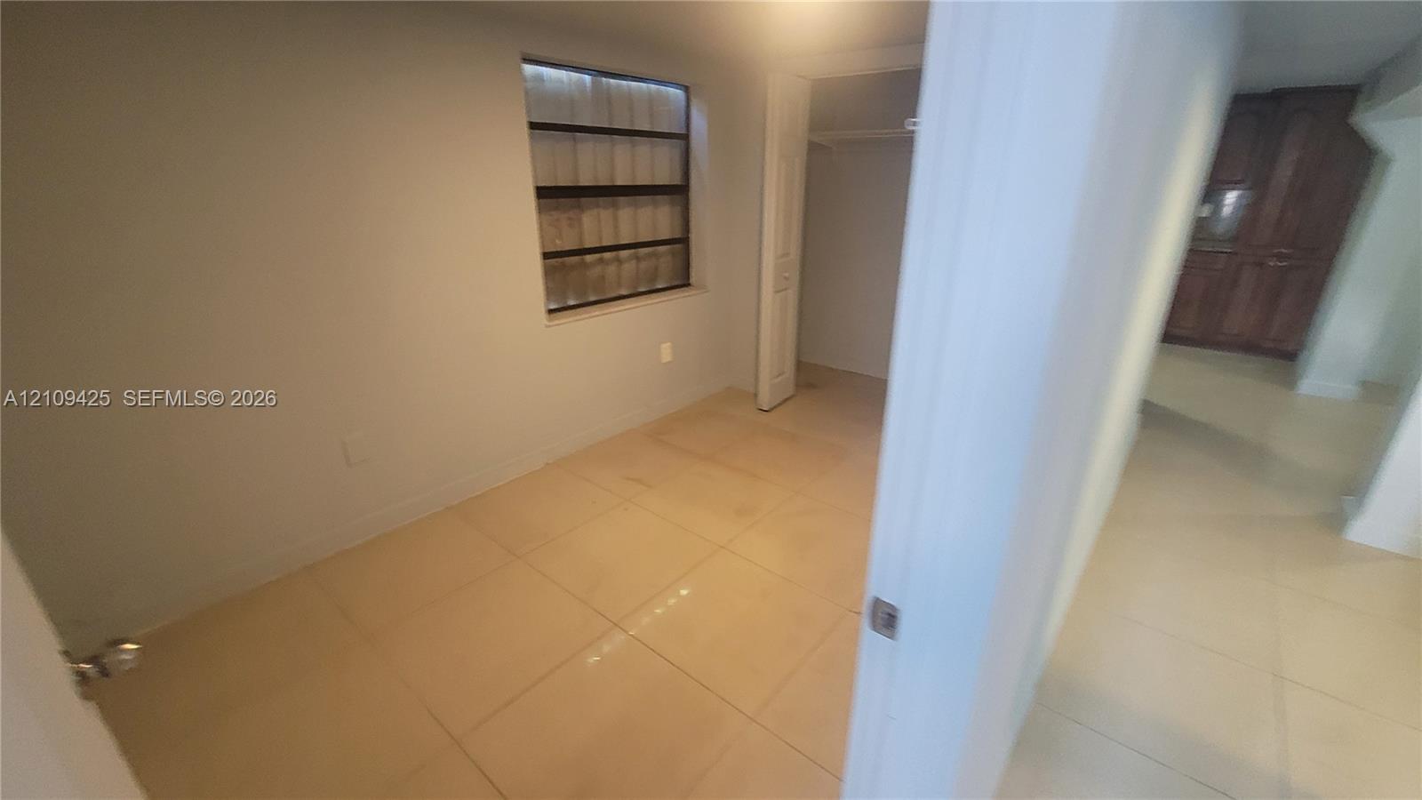 Neutral-toned room featuring large-format tile flooring, a louvered-style window, and a built-in closet with a hinged door