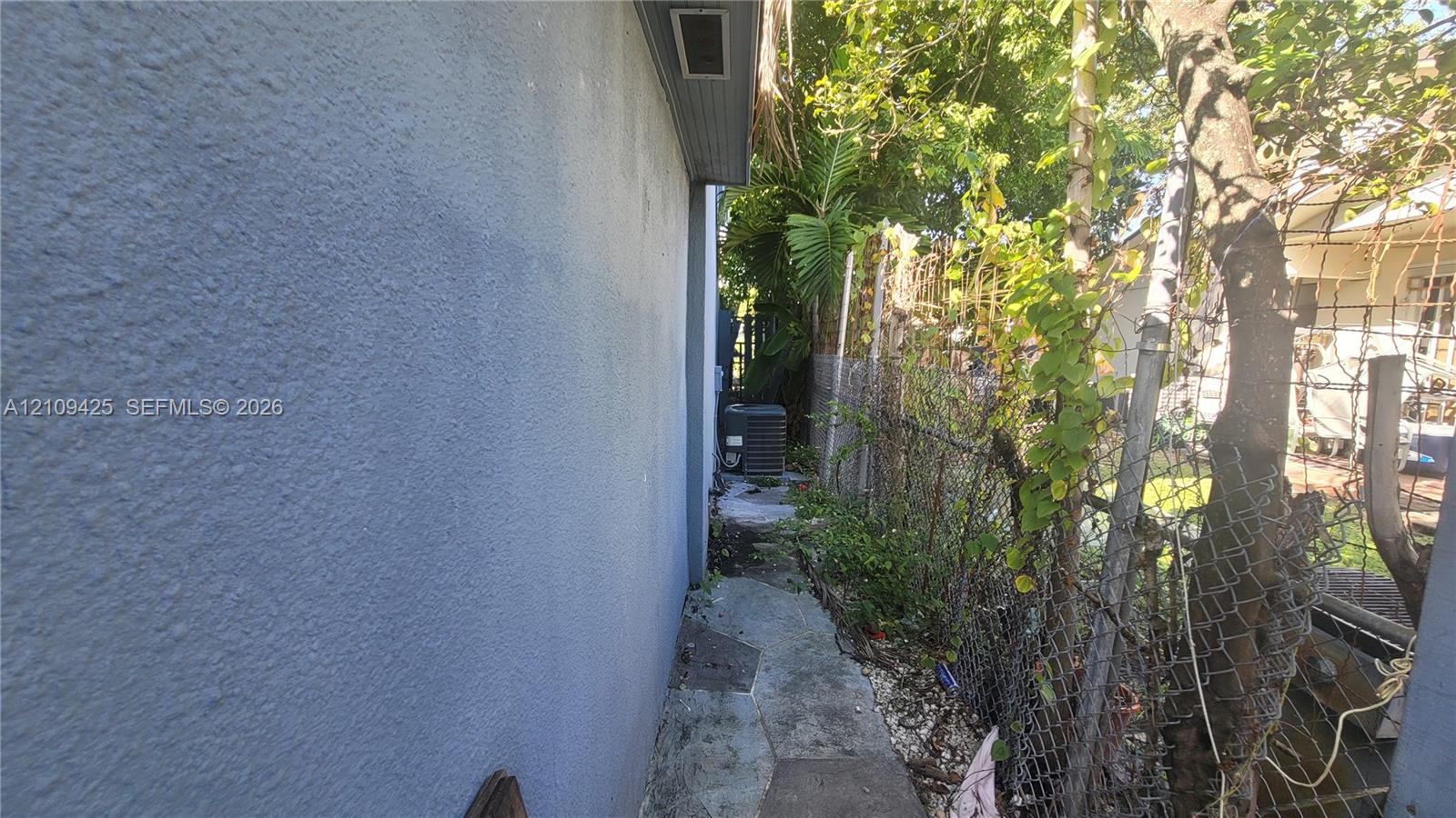 Stucco exterior wall with chain-link perimeter fencing and paved walkway