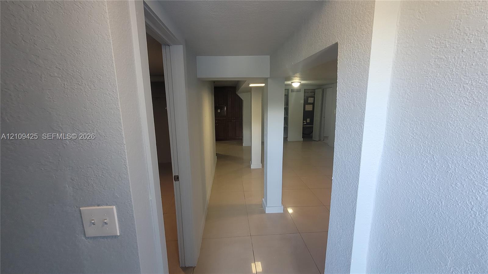 Interior hall featuring neutral-toned large-format tile flooring, textured wall finishes, and a structural support column