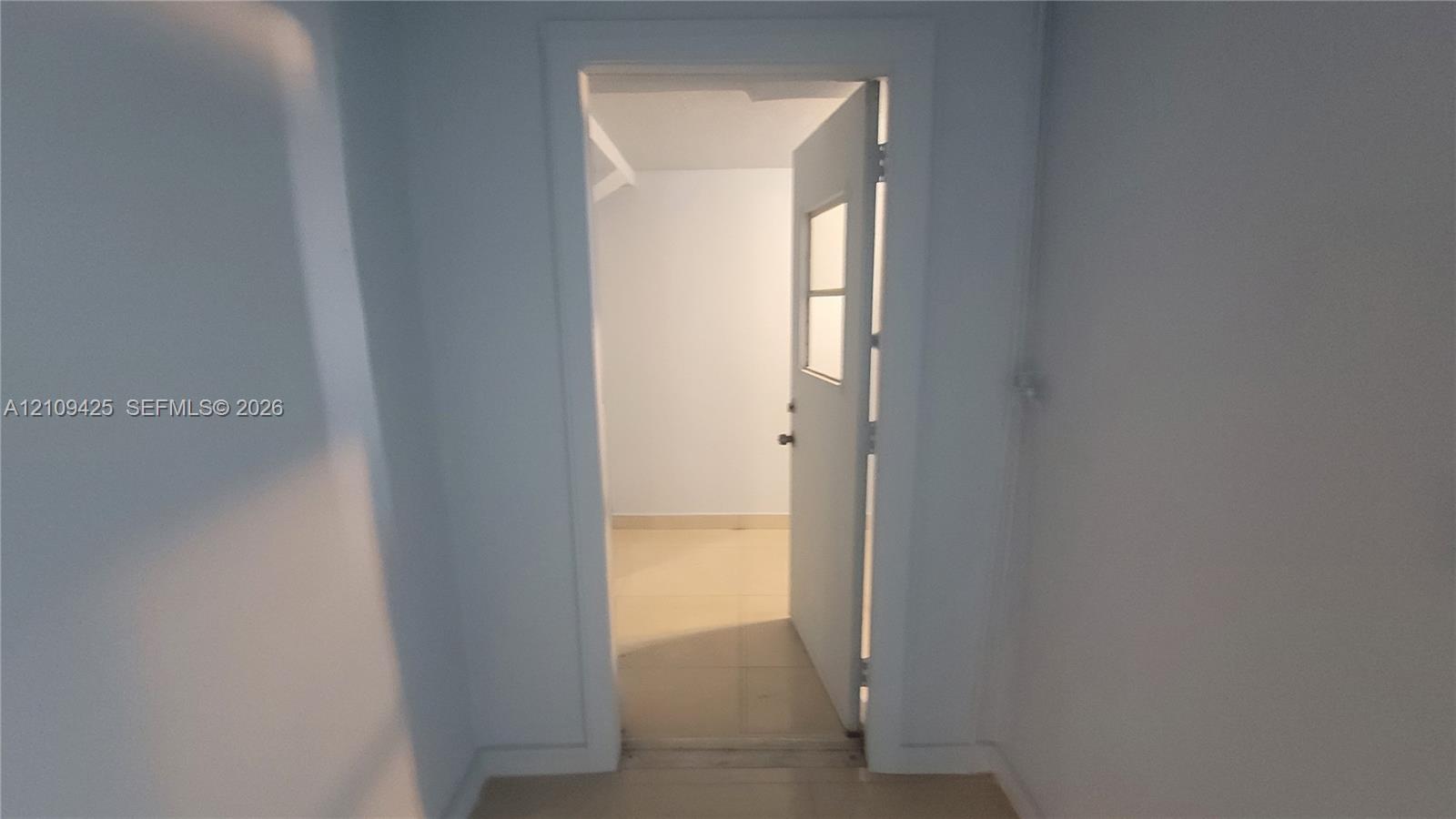 Interior doorway featuring smooth neutral-toned walls, substantial door casing, and a swinging door with a glass pane insert, complemented by light-colored tile flooring