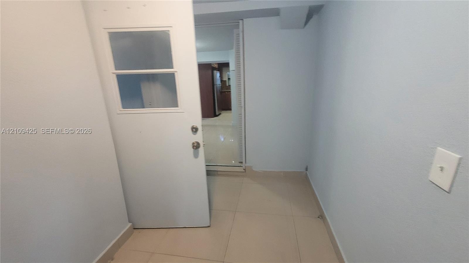 Interior space featuring large-format ceramic tile flooring, a single-lite glass panel door with satin nickel hardware, and smooth-finish walls
