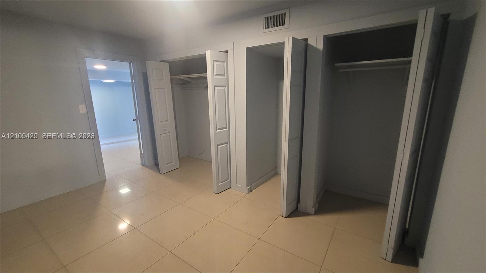 Interior room featuring large-format tile flooring, three white bi-fold closet doors, and built-in shelving