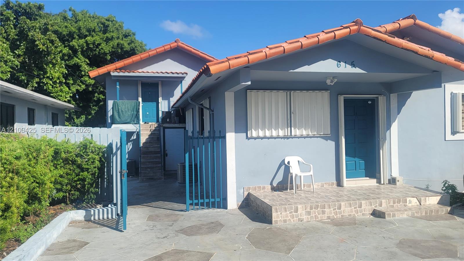Exterior facade featuring a tile roof, covered front porch with tiled flooring, stone-paved driveway, and metal security gate