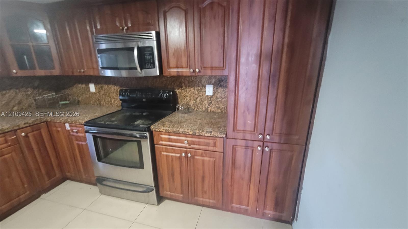 Kitchen featuring wood cabinetry, stone-finish countertops, stainless steel electric range, over-the-range microwave, and tile flooring