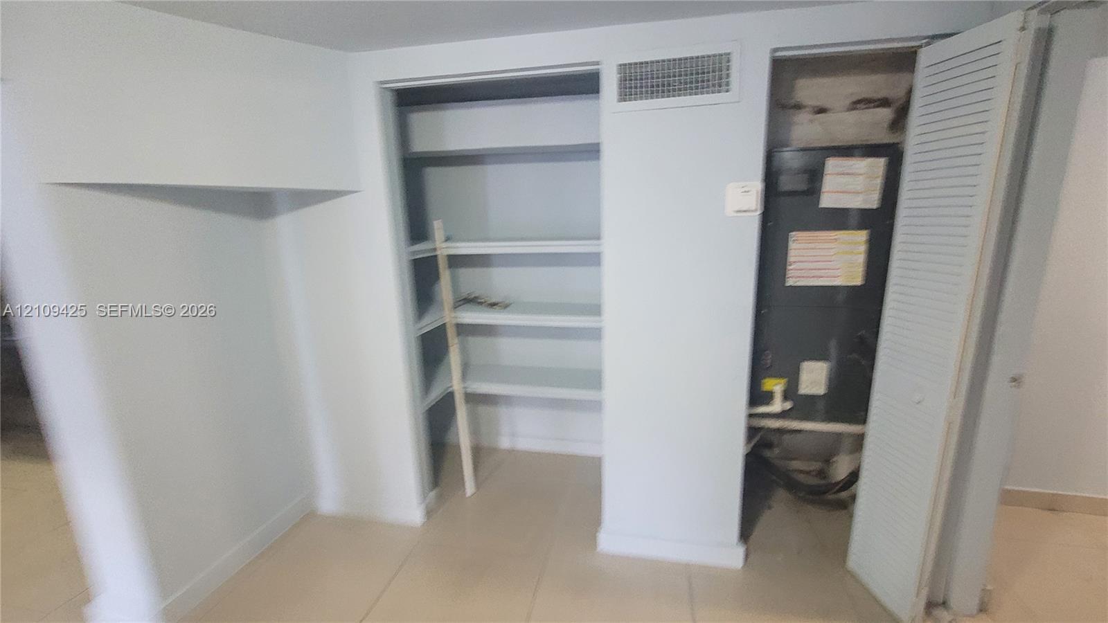 Built-in shelving units and utility closet featuring a mechanical system with louvered door access and tile flooring
