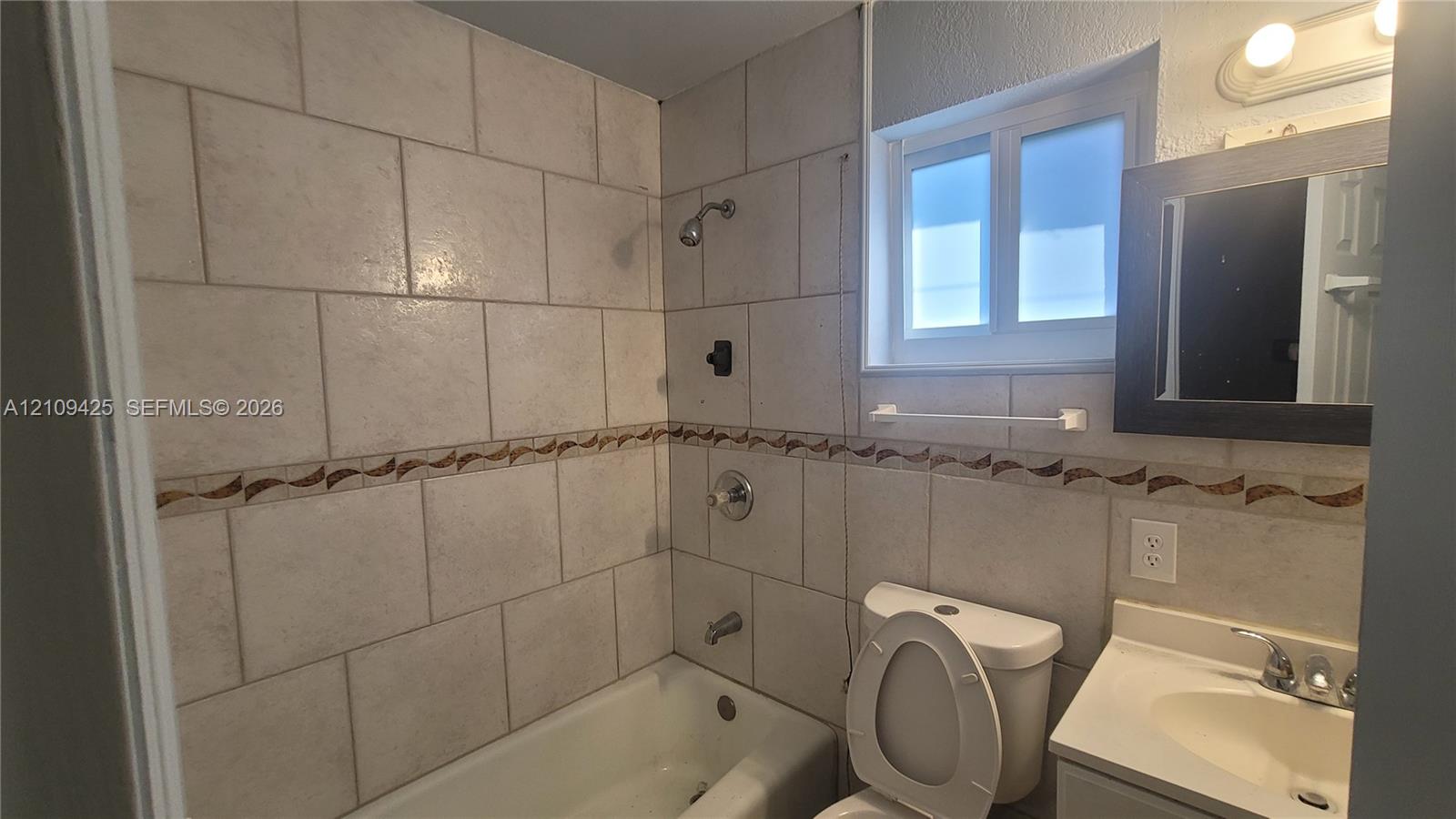 Bathroom featuring a tub-shower combination, wall-mounted vanity with a single basin, inset mirror, and tiled walls with decorative mosaic accents