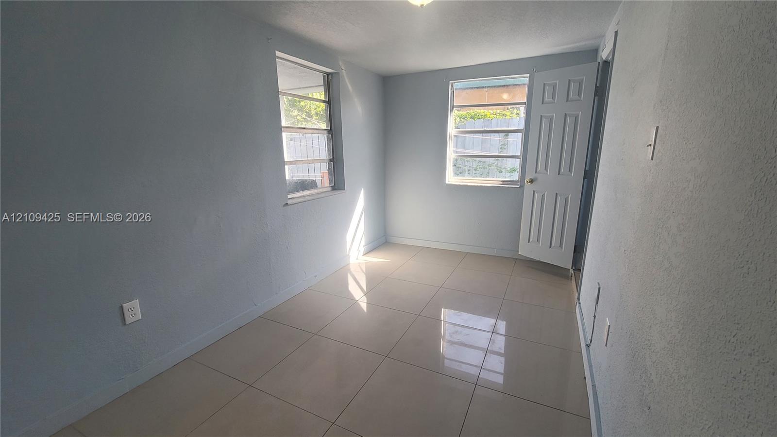 Neutral-toned interior space featuring large-format tile flooring, two multi-pane windows, and a six-panel door