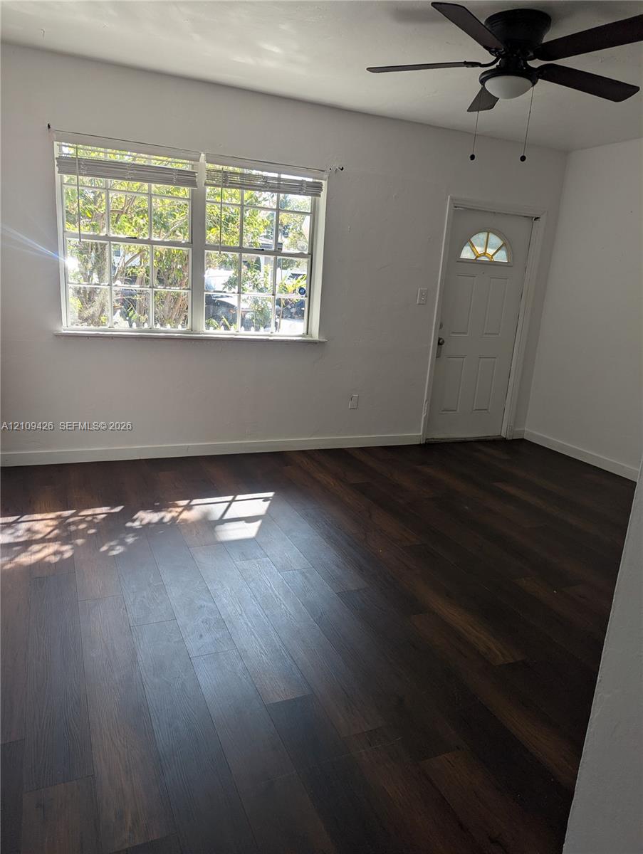 Room featuring dark wood-finish flooring, white walls, a multi-pane window, an exterior door with a semi-circular glass insert, and a ceiling fan