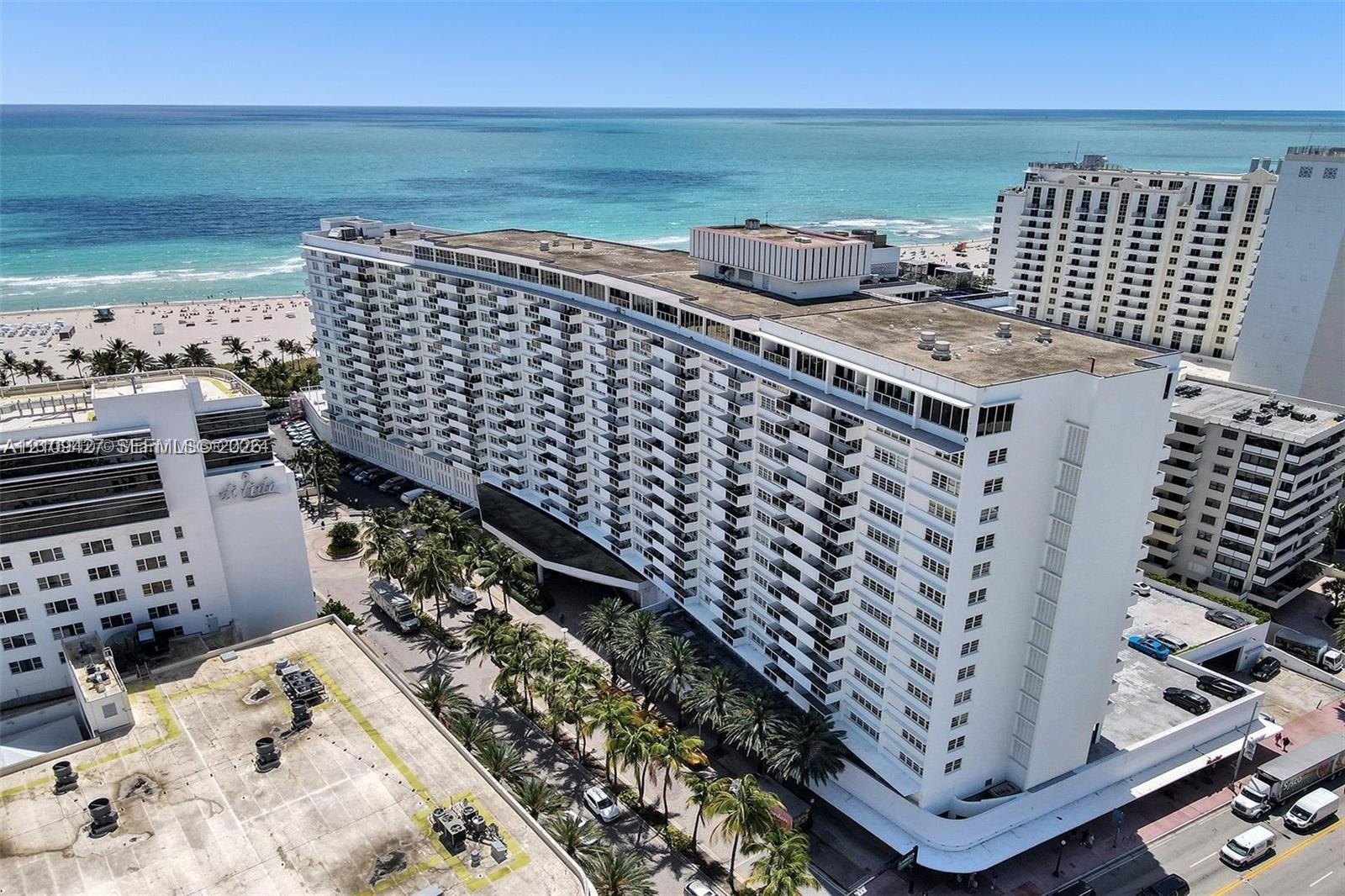 High-rise residential building featuring expansive private balconies, white facade, exterior parking area, and palm tree landscaping