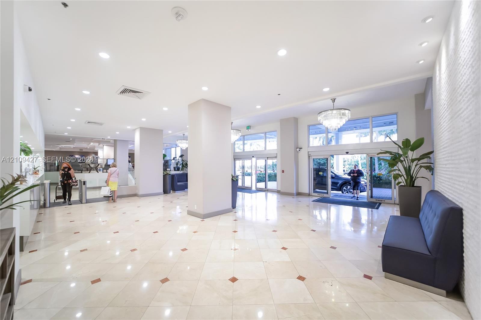 Expansive lobby featuring polished stone tile flooring with decorative inserts, recessed lighting, crystal chandeliers, and floor-to-ceiling glass entry doors