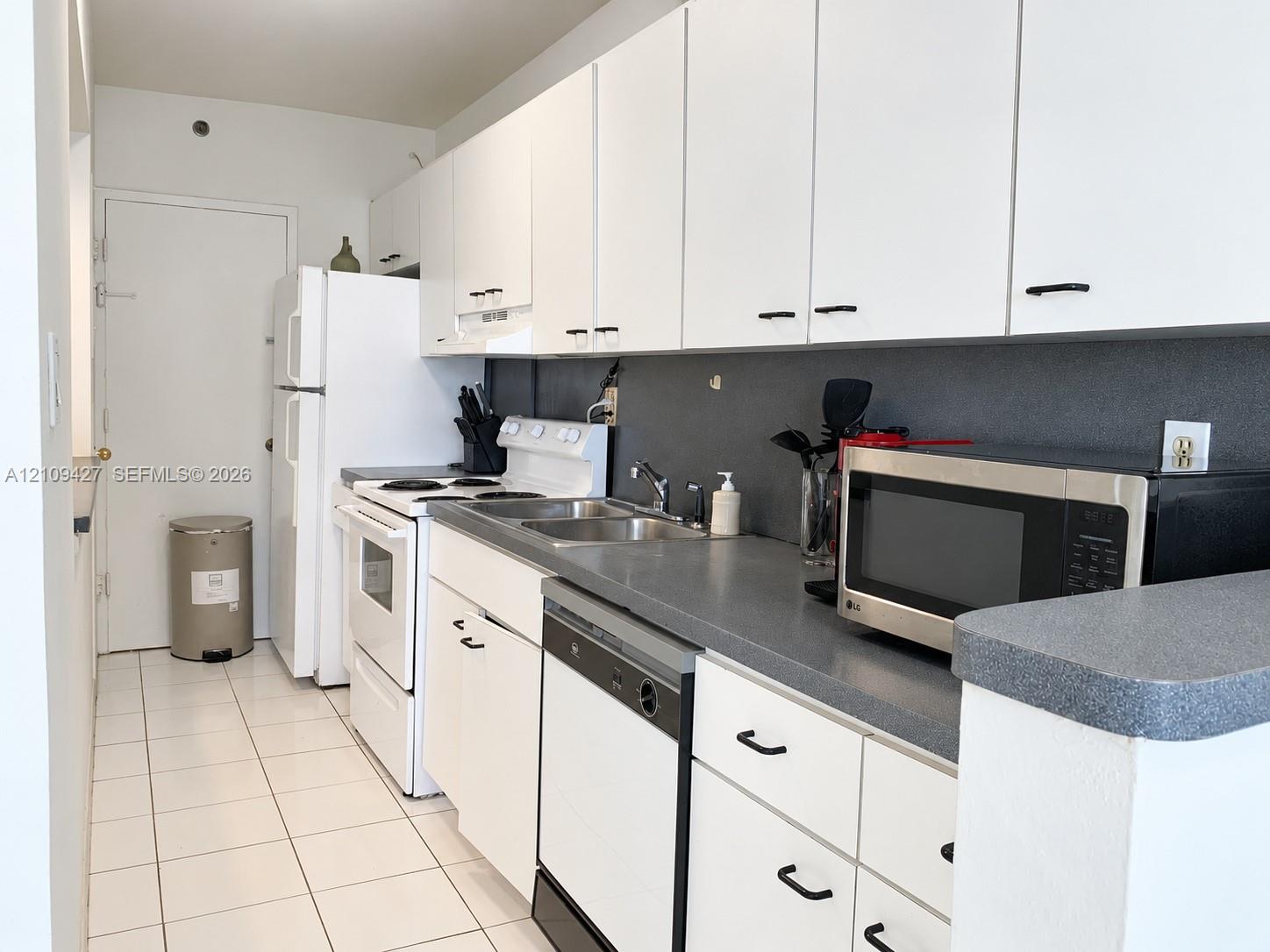 Kitchen featuring white cabinetry, gray solid-surface countertops, a stainless steel double-basin sink, and white ceramic tile flooring