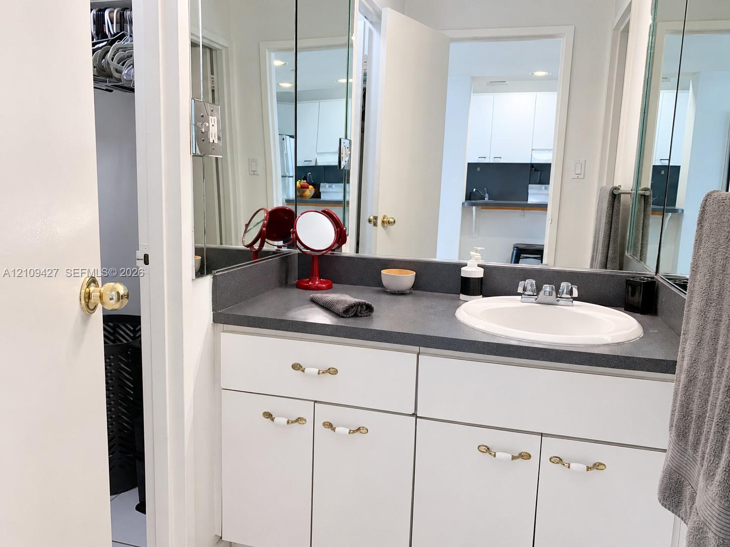 Vanity featuring a solid-surface countertop, integrated basin, dual-handle chrome faucet, and white cabinetry with decorative hardware