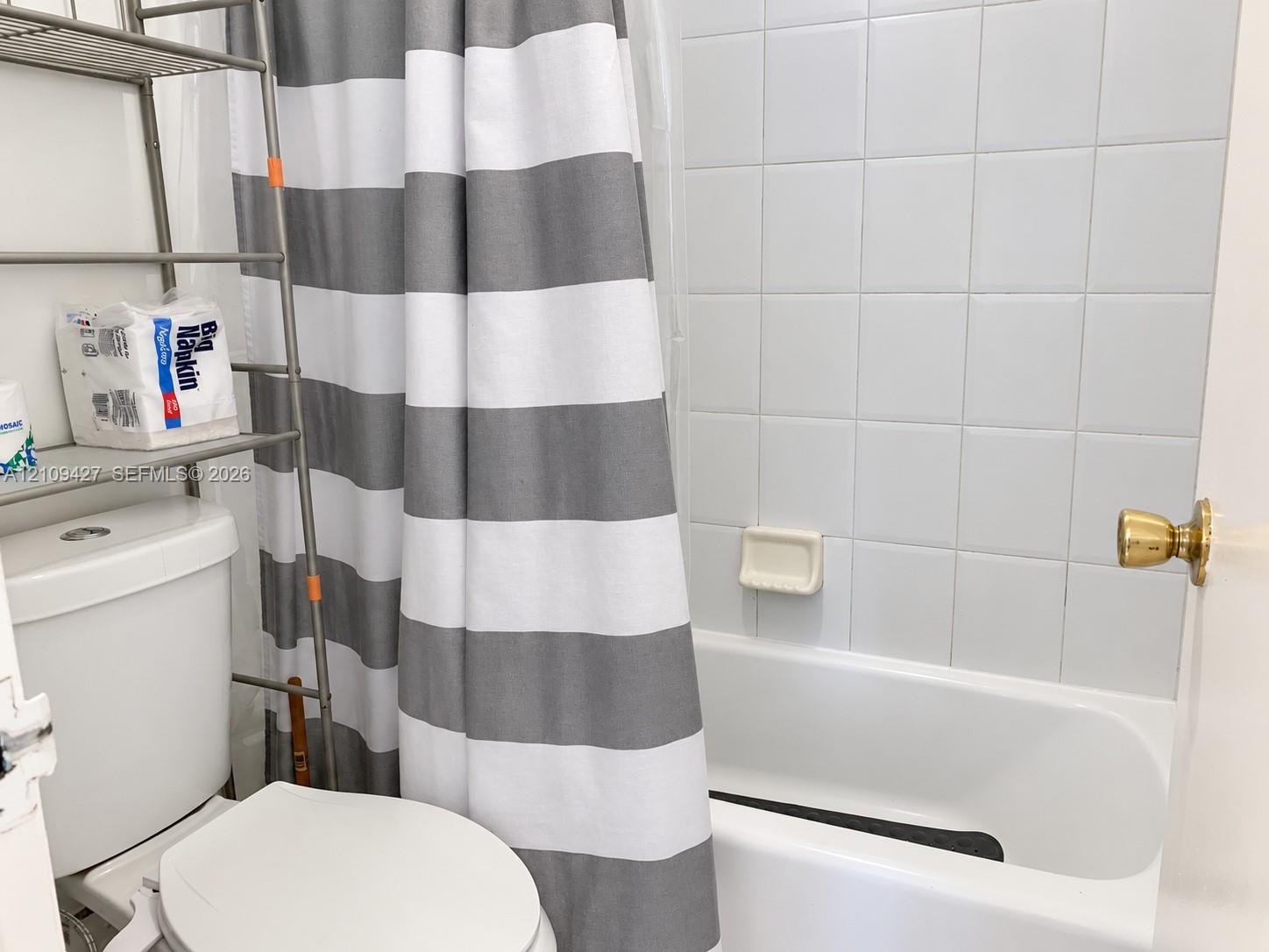Bathroom featuring a white porcelain toilet, a bathtub with a tiled surround, and brass-tone hardware