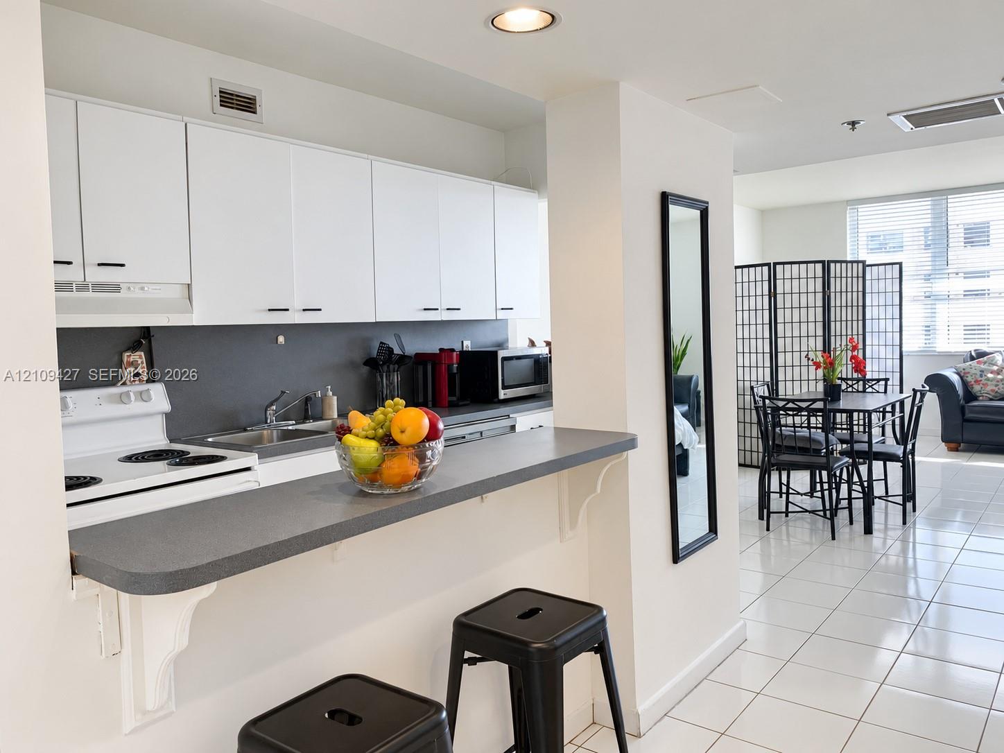 Kitchen featuring white cabinetry, gray solid-surface countertops, integrated breakfast bar, and white tile flooring