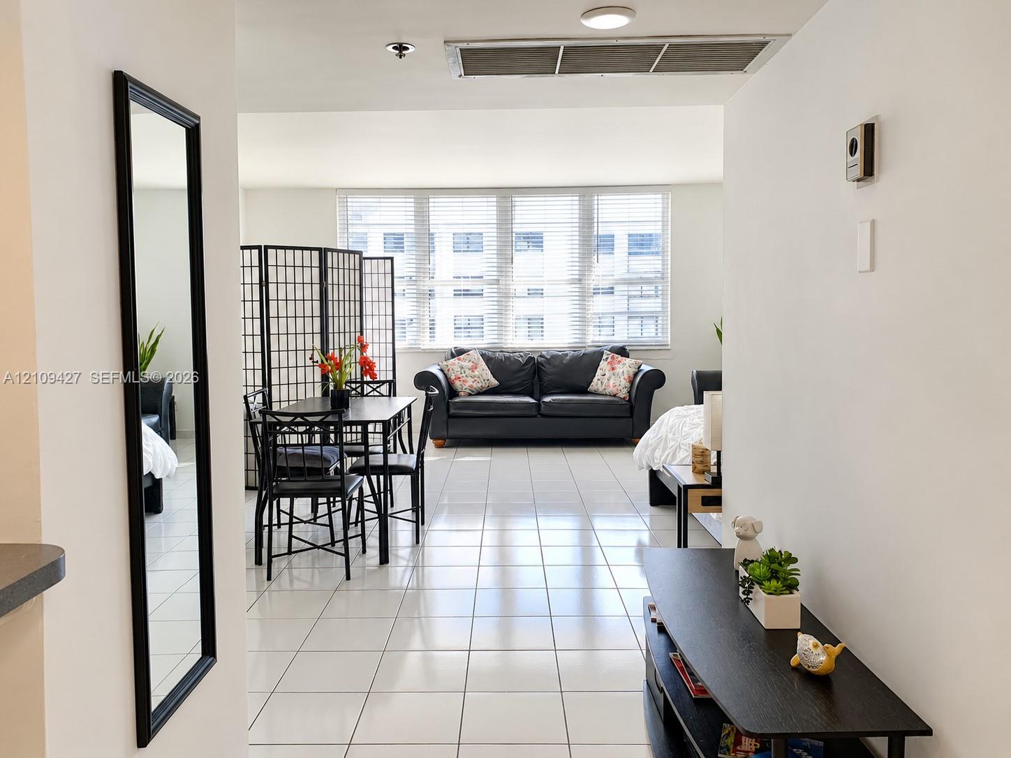 Bright, open-concept interior featuring white ceramic tile flooring and floor-to-ceiling windows with horizontal blinds