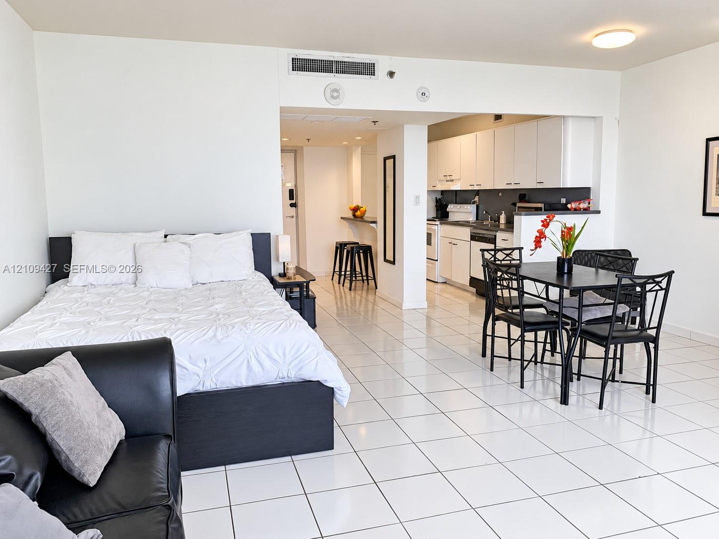 Open-concept living space featuring white ceramic tile flooring, kitchen with white cabinetry, built-in breakfast bar, and flush-mount ceiling lighting