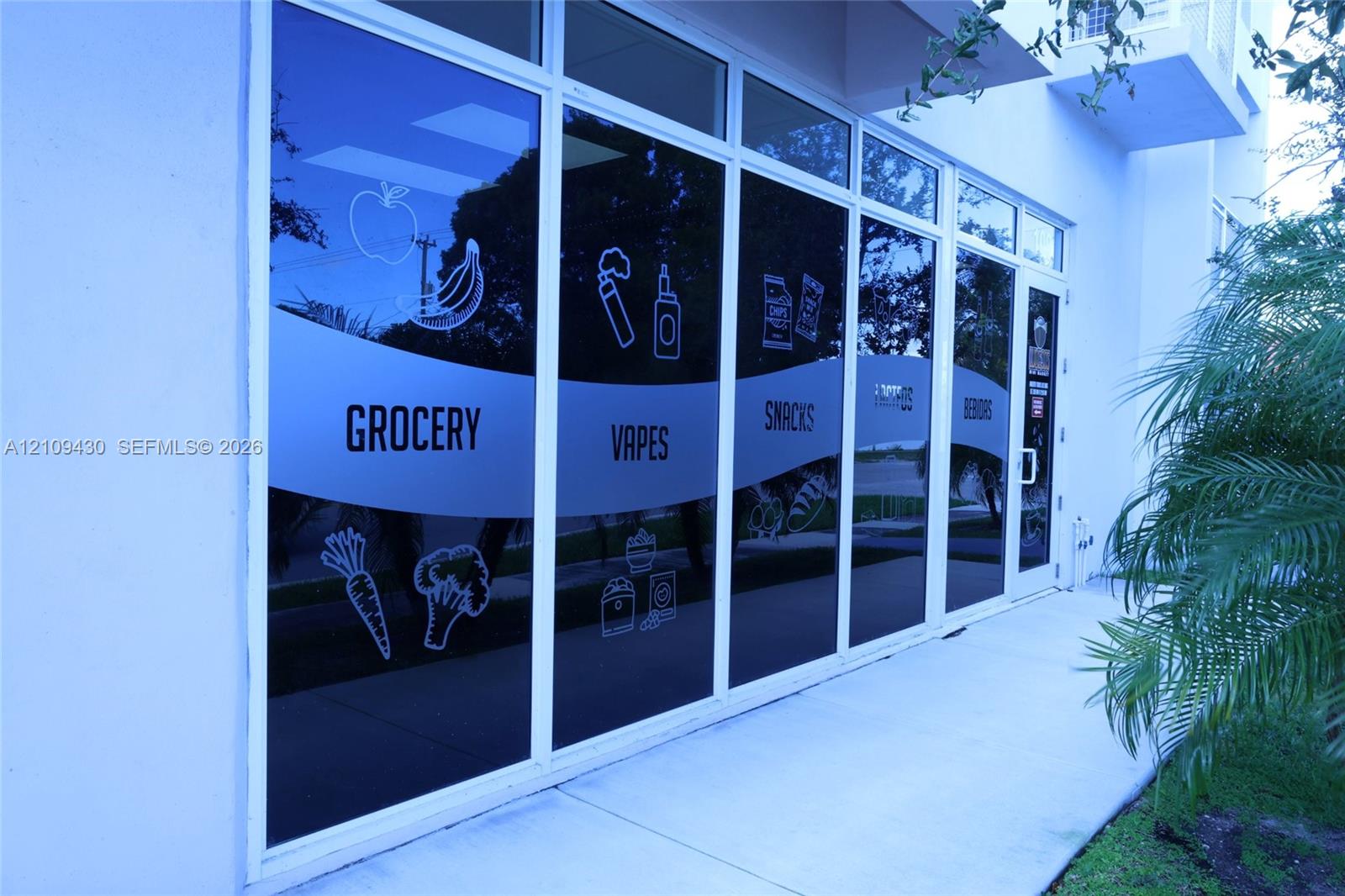 Commercial storefront featuring a white stucco exterior, expansive floor-to-ceiling glass windows, and a dedicated concrete pedestrian walkway