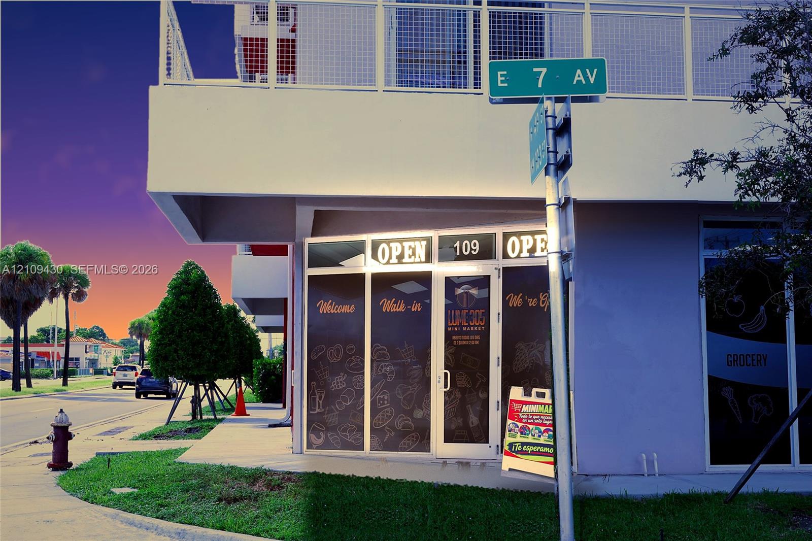 Commercial corner storefront featuring floor-to-ceiling glass display windows, a central glass-panel entry door, and an upper-level balcony with metal mesh railing