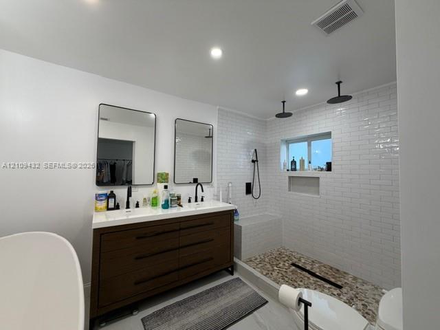 Double vanity with rectangular vessel sinks, dark wood-finish cabinetry, walk-in shower with white subway tile surround, pebble-style flooring, and matte black fixtures
