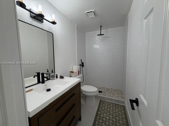 Bathroom featuring a dark wood-finish vanity with a white countertop, matte black fixtures, a walk-in shower with white subway tile, and stone-tiled shower flooring