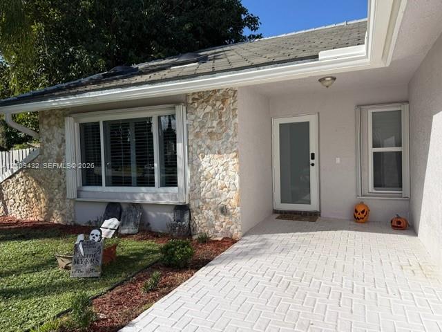 Exterior featuring stone veneer accents, a covered entryway with light-toned herringbone paver flooring, a bay window with multi-pane framing, and a glass-paneled entry door