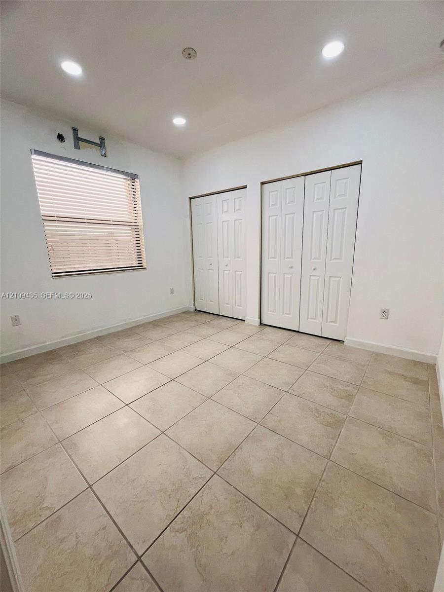 Room featuring neutral tile flooring, recessed ceiling lighting, two bi-fold closets, and a window with horizontal blinds