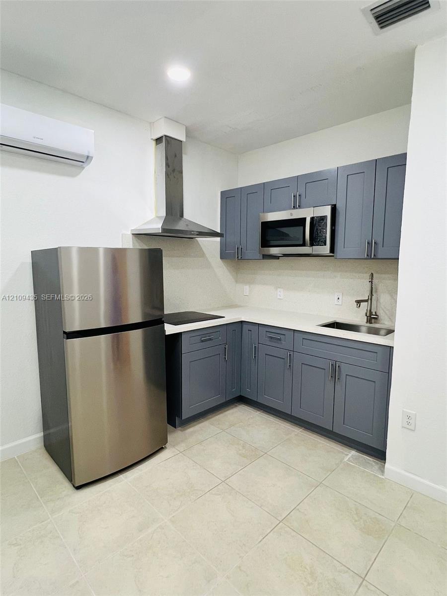 Kitchen featuring grey shaker-style cabinetry, solid-surface countertops, stainless steel appliances, a chimney-style range hood, and tile flooring