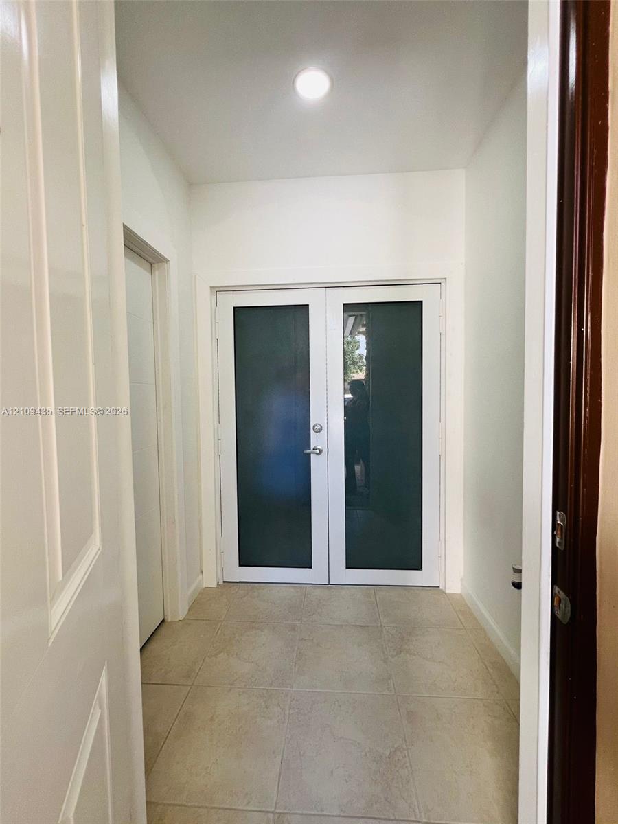 Double-entry doors with opaque glass panels, light-toned ceramic tile flooring, and a ceiling-mounted flush light fixture