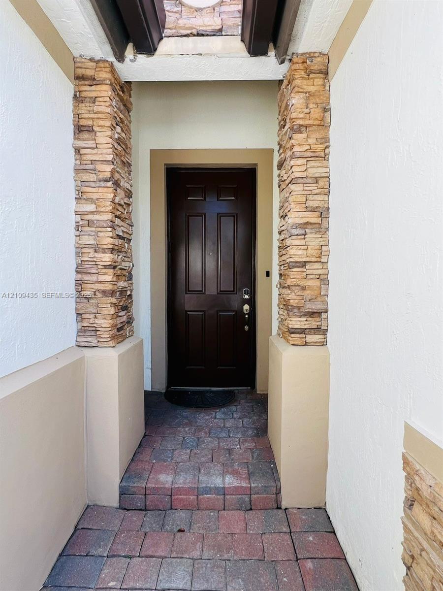Covered entryway featuring stone veneer columns, a multi-paneled dark wood-finish door, and paver stone flooring