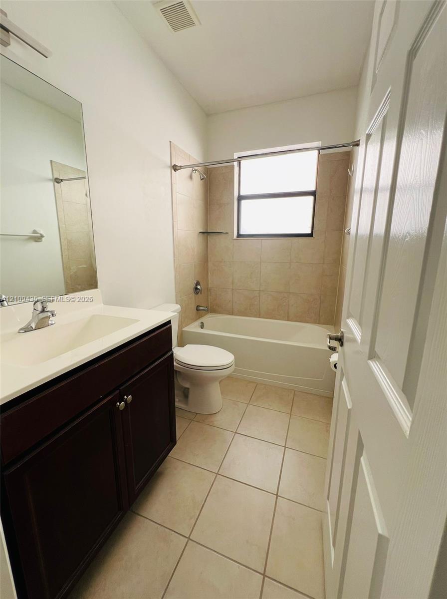 Bathroom featuring a vanity with a white integrated countertop, dark cabinetry, tile flooring, and a tub-shower combination with tiled walls