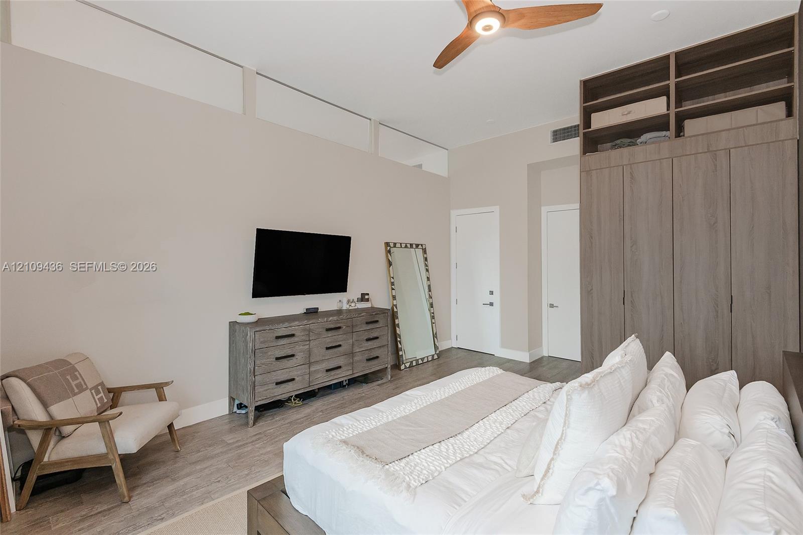 Floor-to-ceiling built-in wooden cabinetry, clerestory windows, wood-finish flooring, and a modern three-blade ceiling fan with integrated lighting