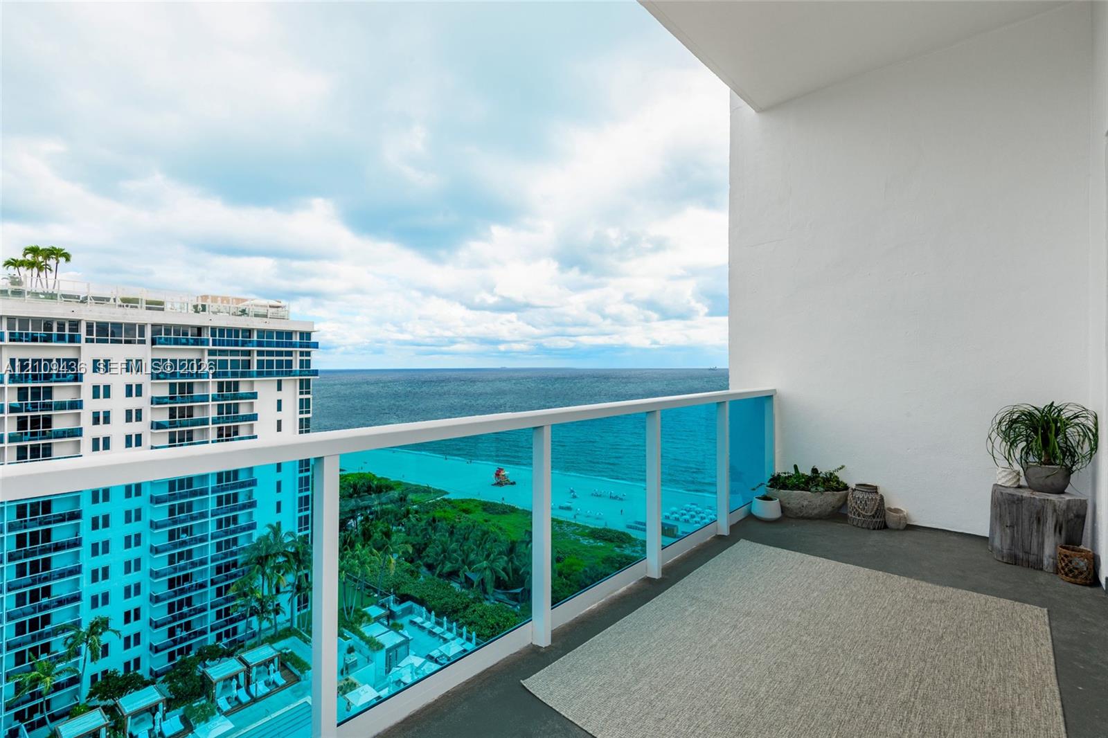 Private balcony featuring a glass-panel railing and concrete flooring, showcasing an expansive ocean and coastal panorama