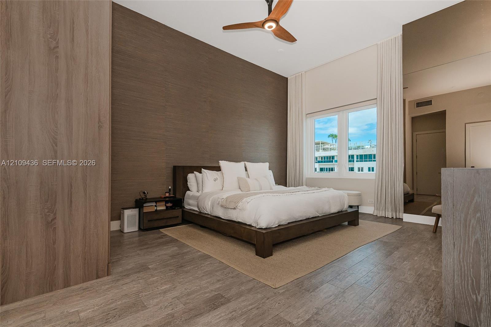 High-ceiling room featuring wood-finish flooring, a full-height decorative wood-paneled wall, a modern three-blade ceiling fan, and a floor-to-ceiling mirror panel