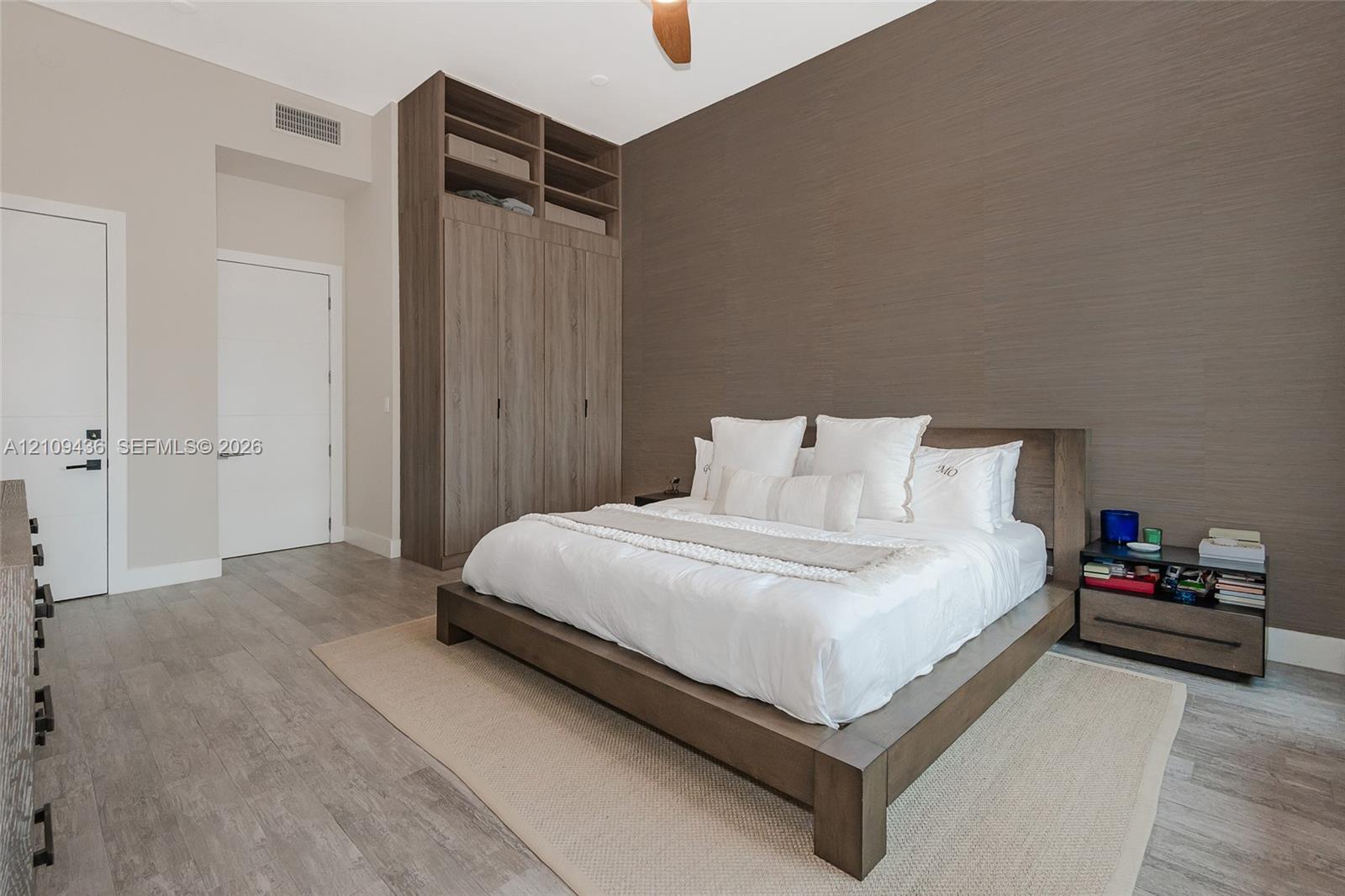 Floor-to-ceiling built-in wooden cabinetry, textured accent wall, wood-finish flooring, and a ceiling fan