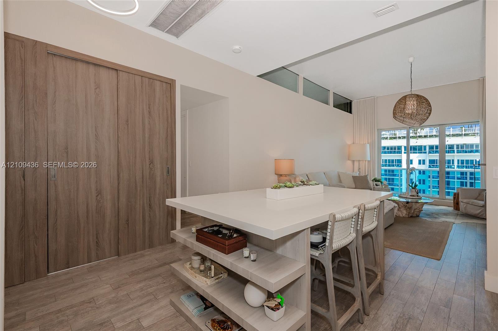 Central island with integrated shelving and solid surface countertop, wood-finish flooring, floor-to-ceiling wood-finish sliding doors, and clerestory windows