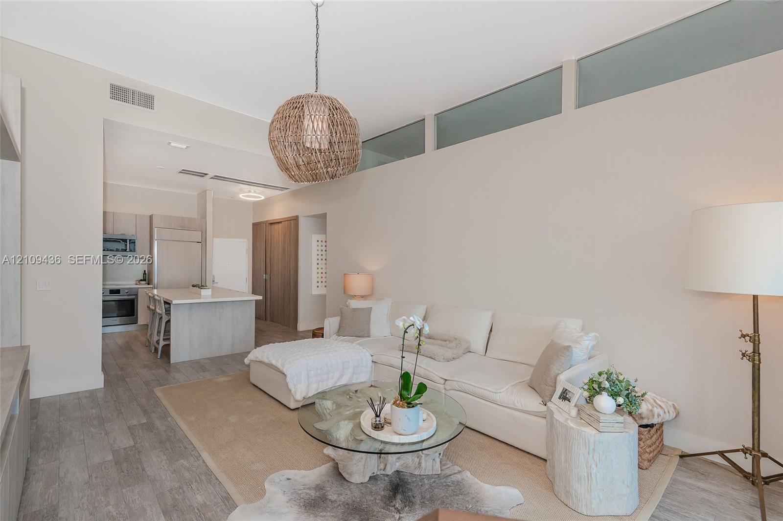 High-ceiling living area featuring clerestory windows, wood-finish flooring, a woven pendant light fixture, and an integrated kitchen with a stone-surface island