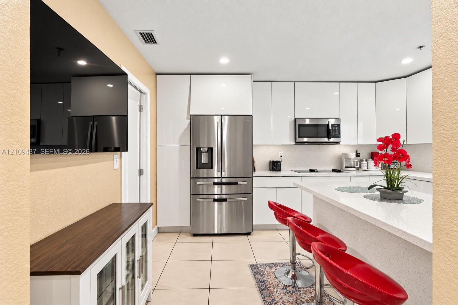 Kitchen featuring white high-gloss cabinetry, stainless steel appliances, quartz countertops, a kitchen island, and ceramic tile flooring Kitchen featuring white high-gloss cabinetry, stainless steel appliances, quartz countertops, a kitchen island, and ceramic tile flooring