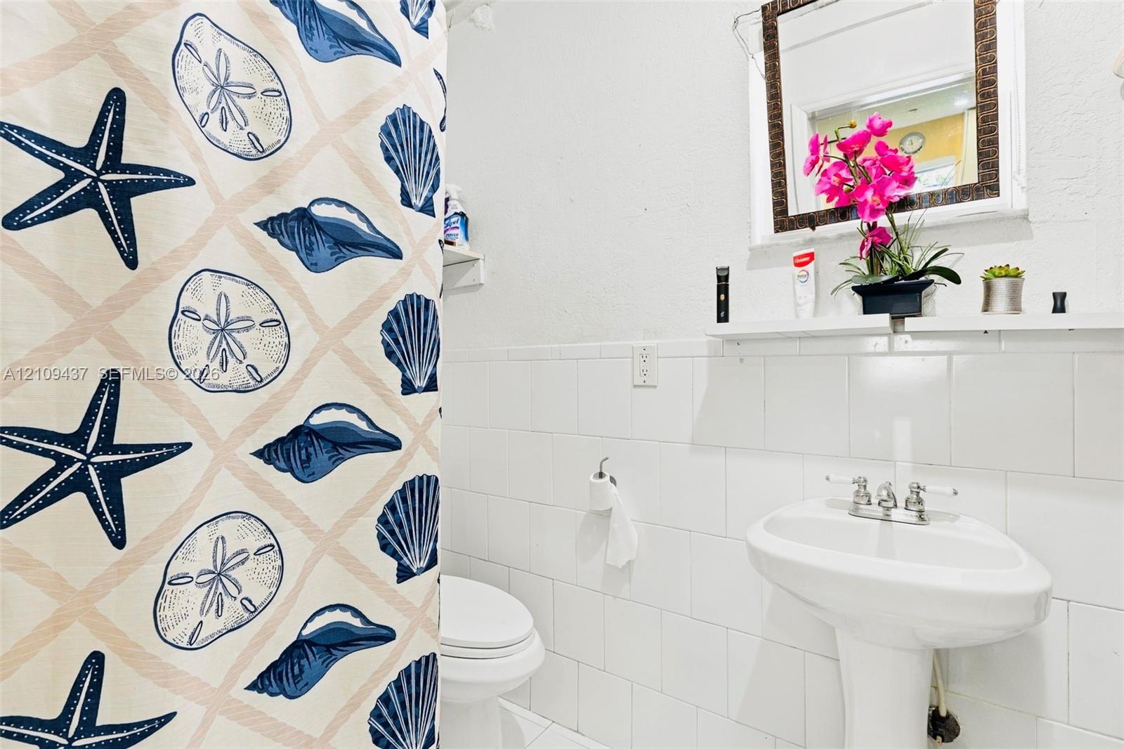 Bathroom featuring a pedestal sink with a dual-handle faucet, white tile wall surround, and a built-in wall shelf