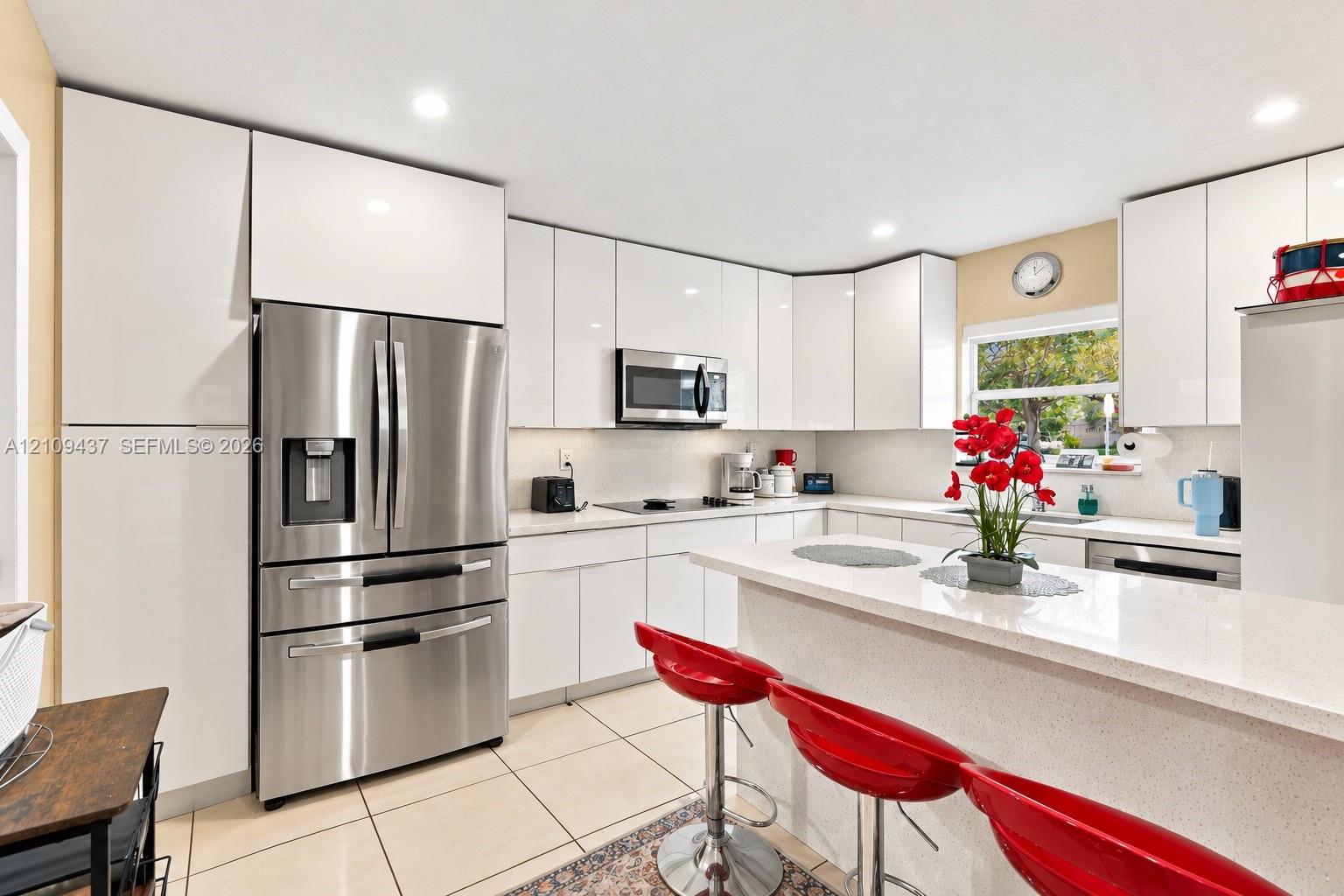 Kitchen featuring high-gloss white cabinetry, solid surface countertops, stainless steel appliances, recessed lighting, and tile flooring Kitchen featuring high-gloss white cabinetry, solid surface countertops, stainless steel appliances, recessed lighting, and tile flooring