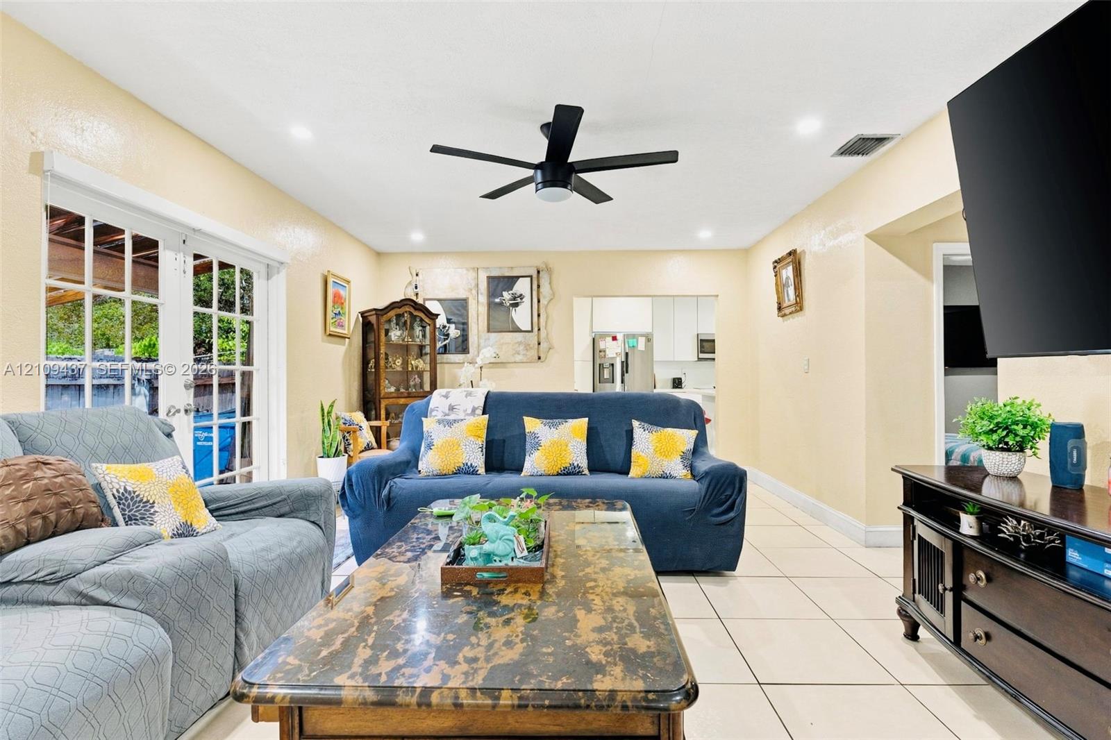 Living area featuring large format neutral tile flooring, recessed lighting, a modern matte black ceiling fan, and multi-panel glass French doors