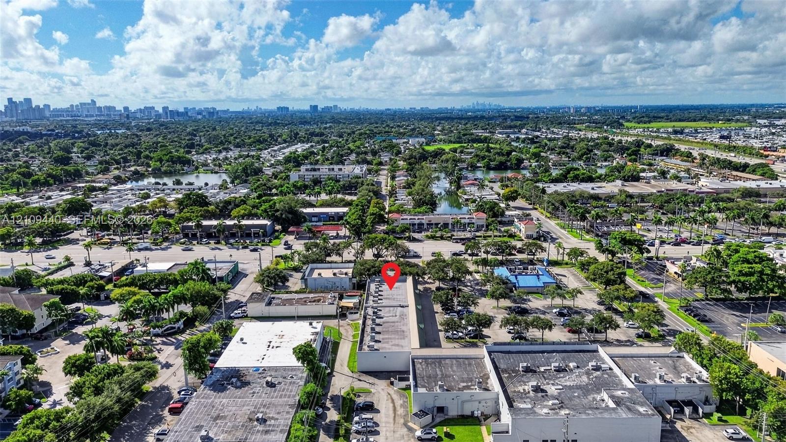 Aerial perspective of a commercial property featuring a flat-roof structure with rooftop HVAC units, multiple paved parking areas, and frontage on a primary thoroughfare