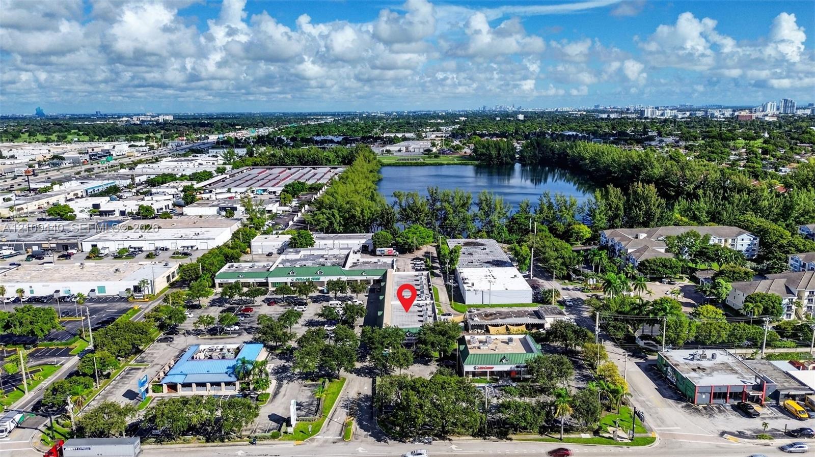 Aerial perspective of a multi-unit commercial property featuring a flat roof structure, paved parking area, and mature landscaping