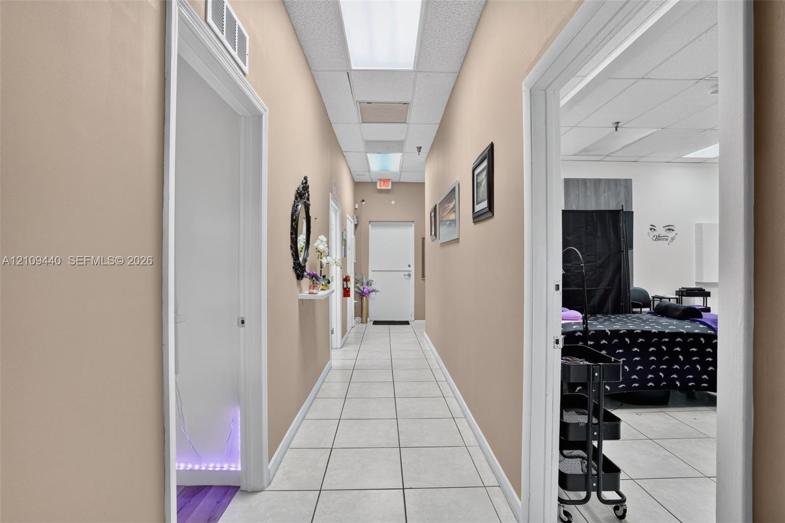 Interior hallway featuring white tile flooring, recessed drop-ceiling lighting, and multiple entryways with clean white trim