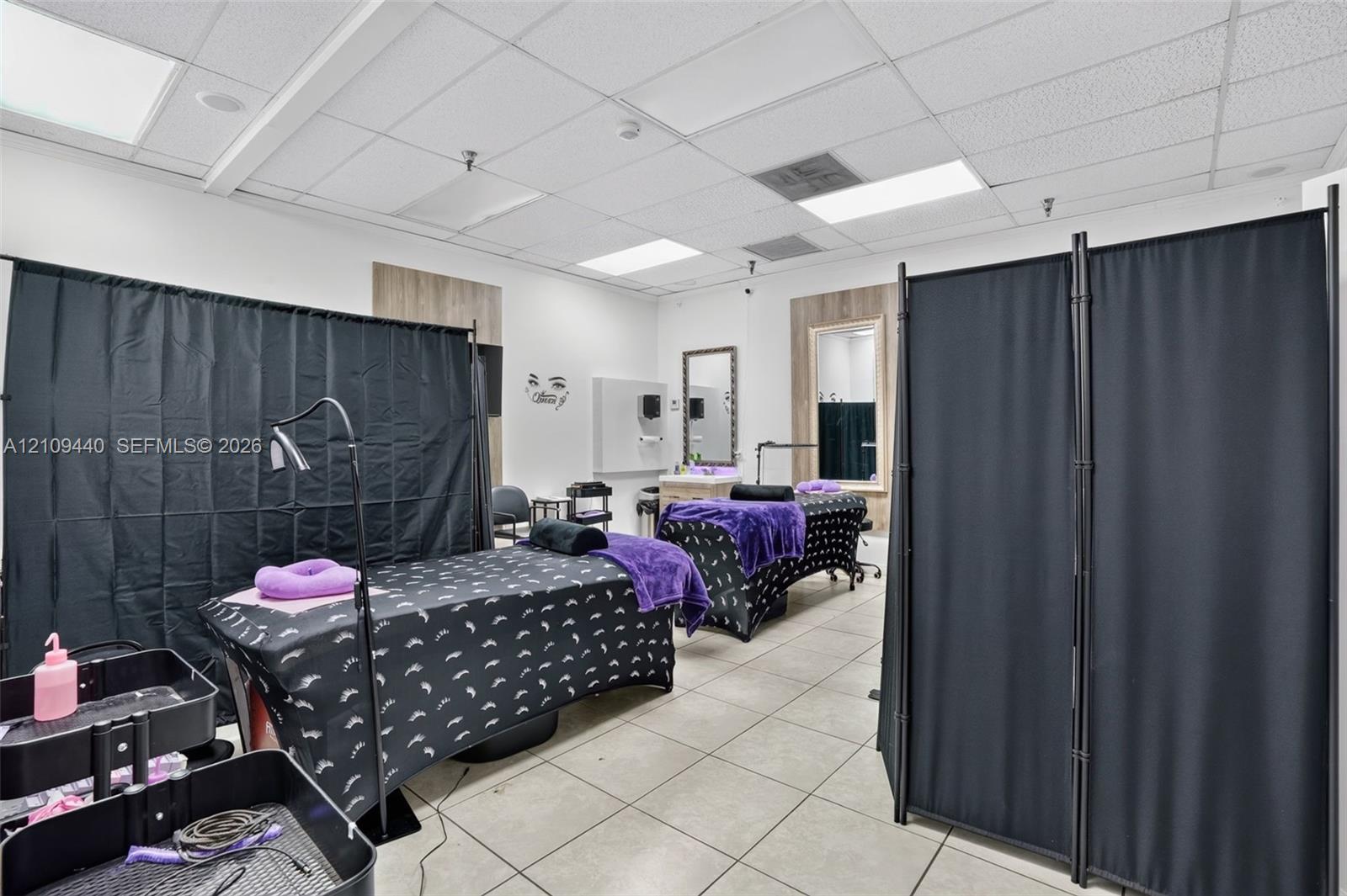 Commercial space featuring neutral tile flooring, recessed drop-ceiling lighting, and wall-mounted vanity mirrors with wood-finish trim